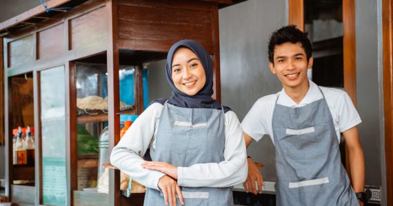 veiled woman and young man wearing an apron smiling veiled woman and young man wearing an apron smiling while selling at a chicken noodle cart